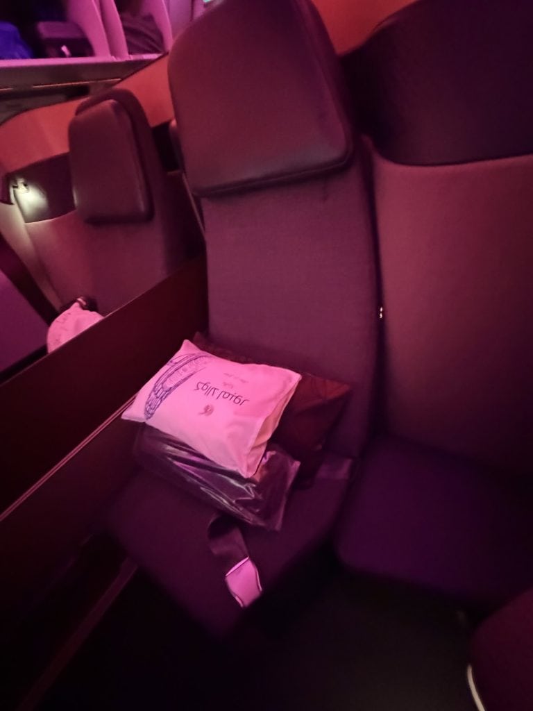 Bus seat with a pink bag and personal belongings in a dimly lit travel setting.