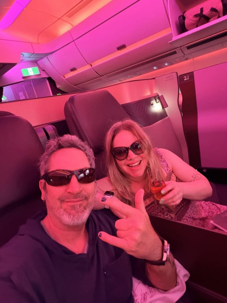Travelers enjoying a flight in a modern airplane cabin with vibrant pink lighting.
