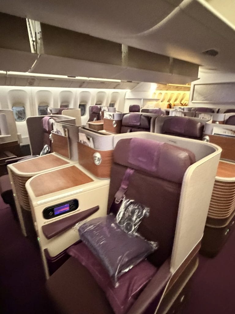 Business class airplane seat with privacy divider and plush pillows.