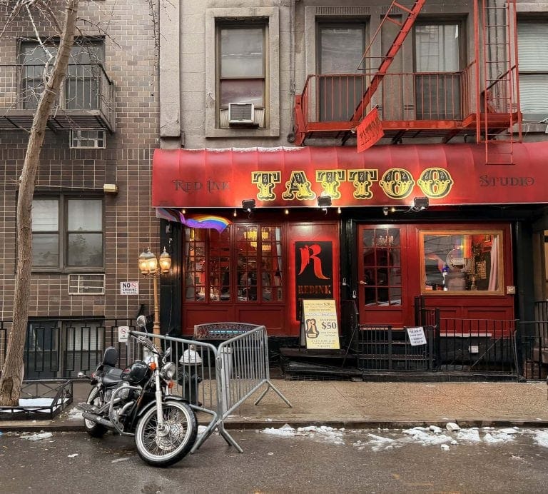 Tattoo studio storefront with red facade and neon signs in NYC.
