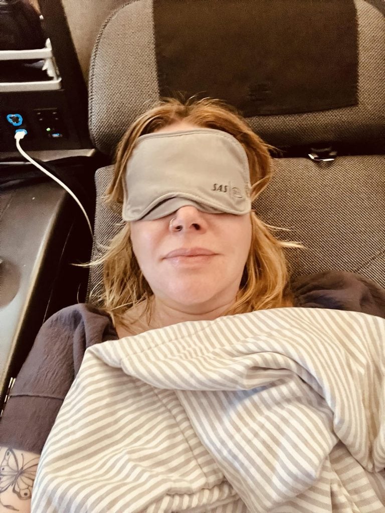 Woman resting with sleep mask on airplane, traveling comfortably.