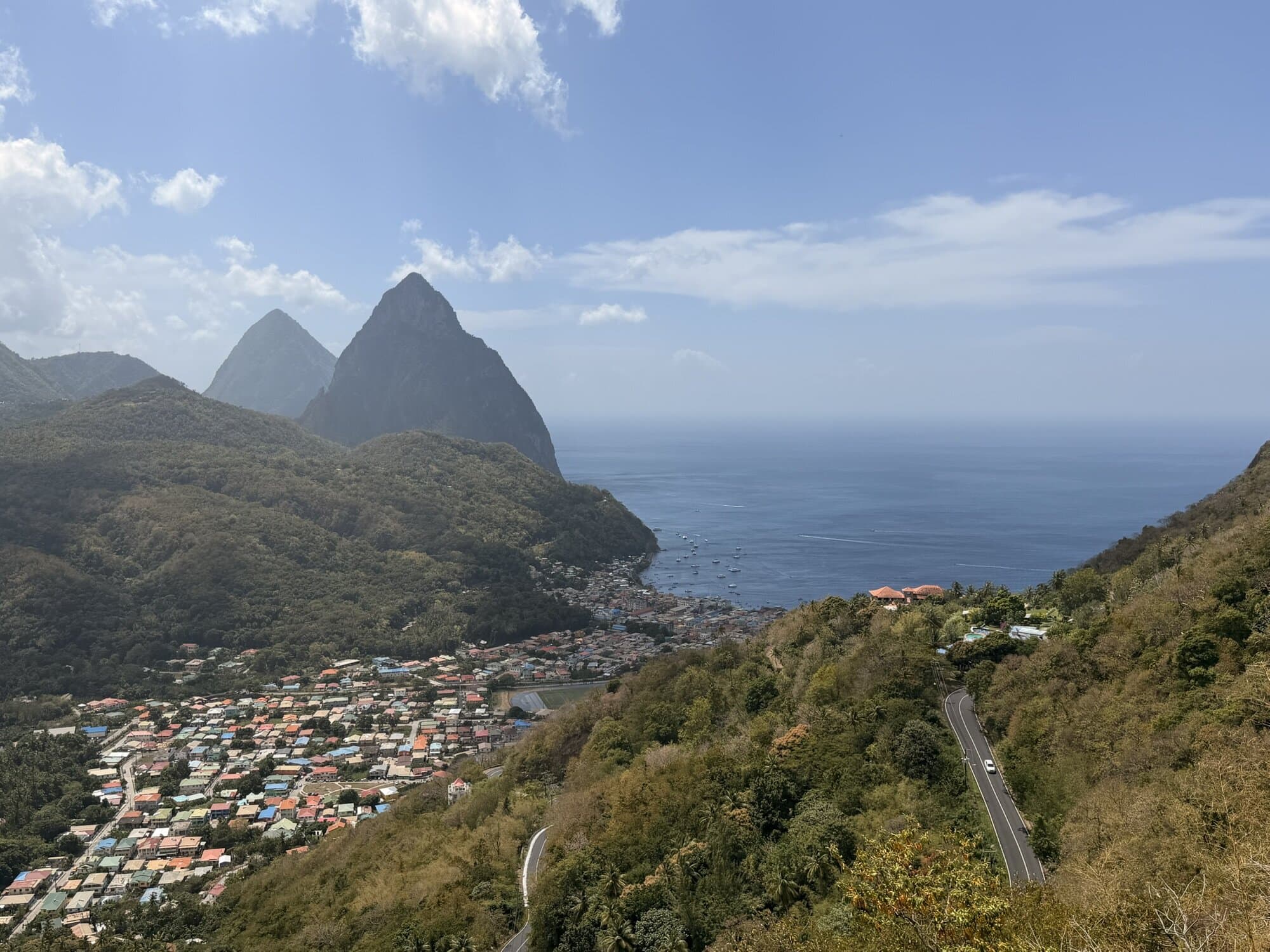 Mountain and coastal village view with lush greenery and ocean in the background.