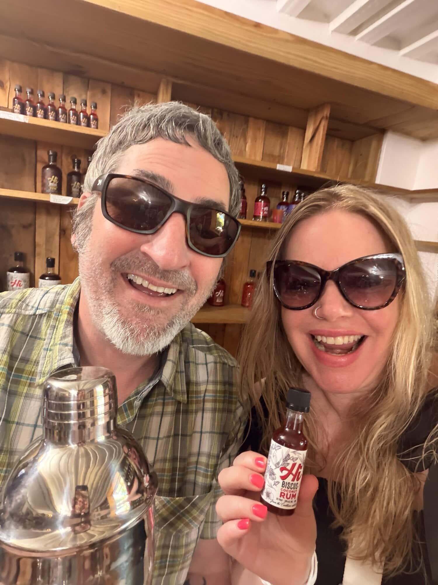 Happy couple enjoying travel, holding a small bottle, in a cozy bar setting.