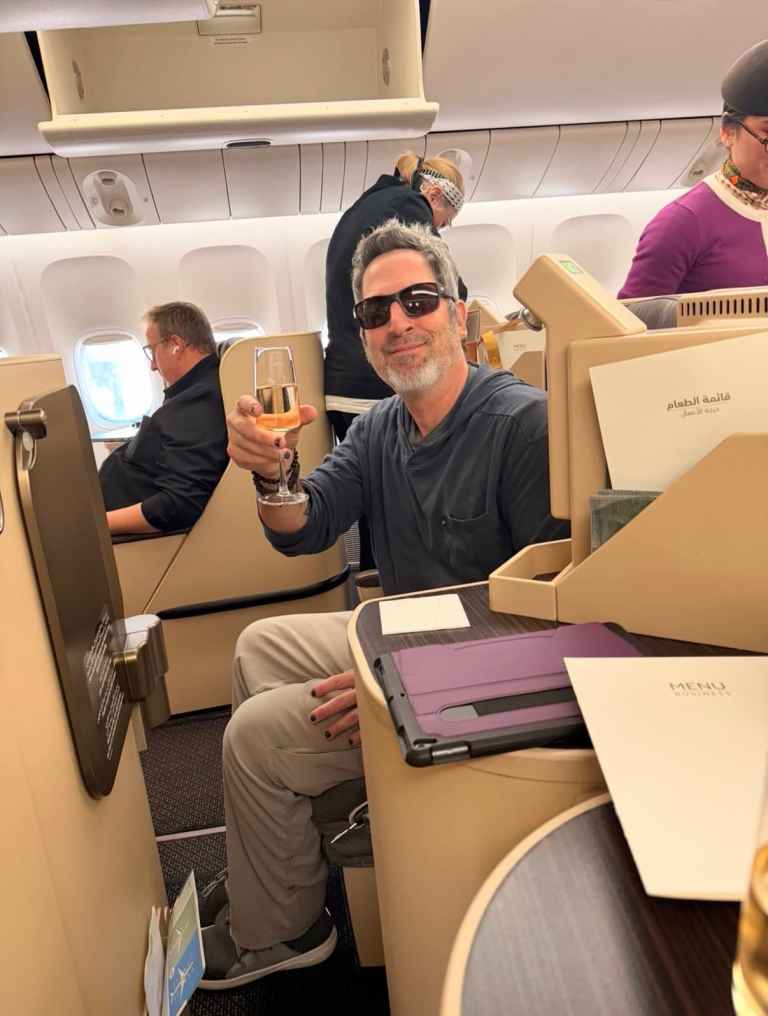 Man with sunglasses holding a glass of wine on a plane.