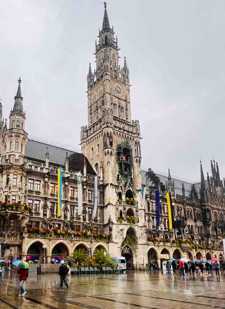 Gothic Town Hall with clock tower in Munich, Germany, during rainy weather with visitors holding umb.