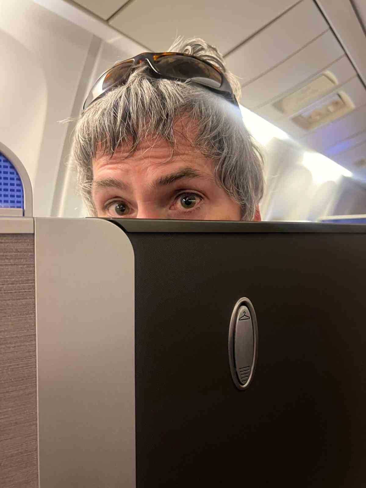Man with gray hair and sunglasses looking over airplane seat.