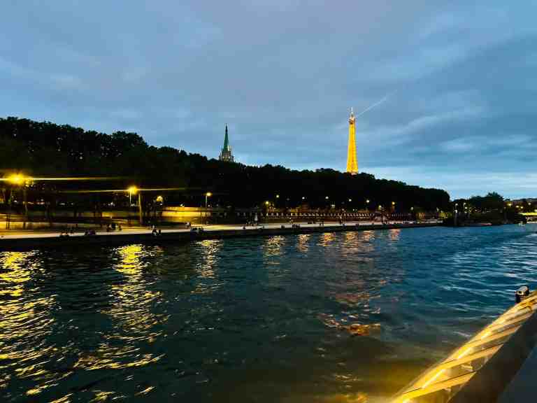 View of Paris skyline with Eiffel Tower and city lights reflected on the river at dusk.