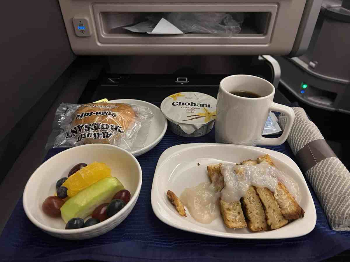 Travel meal on an airplane tray with bread, fruit, and coffee.