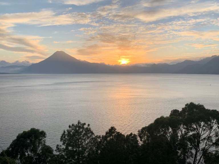 Scenic sunset over a volcanic lake with mountains and trees in foreground.