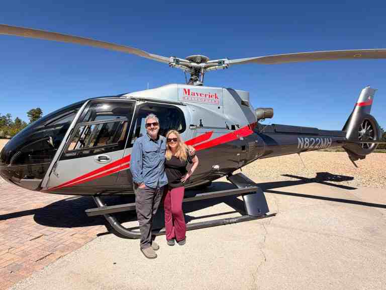 Happy travelers standing next to a Maverick helicopter during a scenic tour.