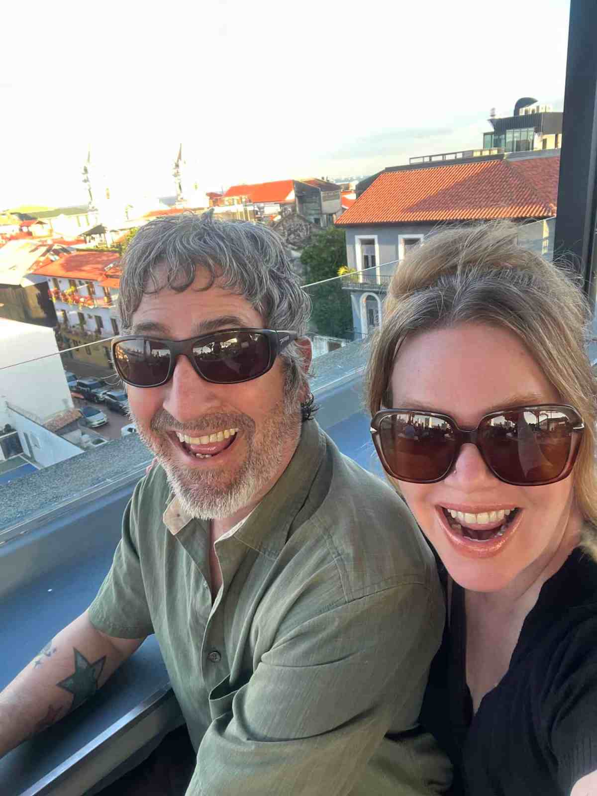 LiAnn and Theo smiling on balcony with city view in background.