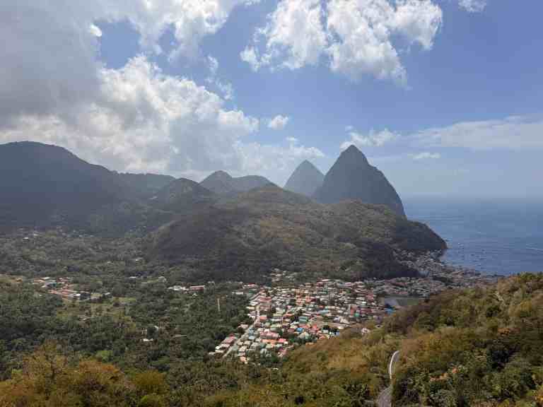 Scenic view of mountains, village, and ocean under partly cloudy sky.