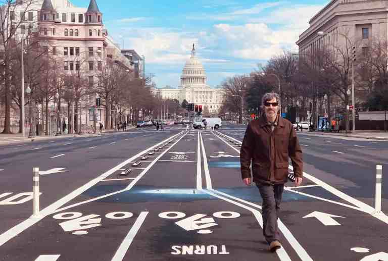 Travelers walking on empty street with US Capitol in background.