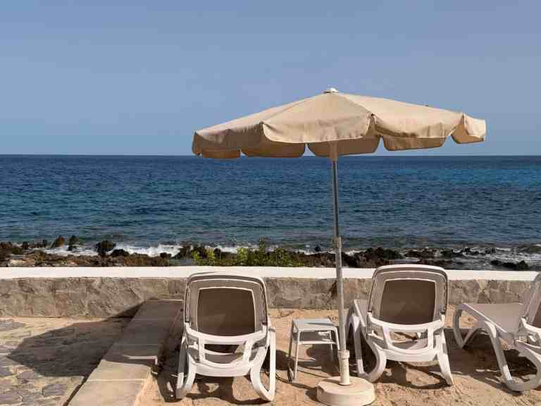 Beach scene with umbrella, lounge chairs, and ocean view.