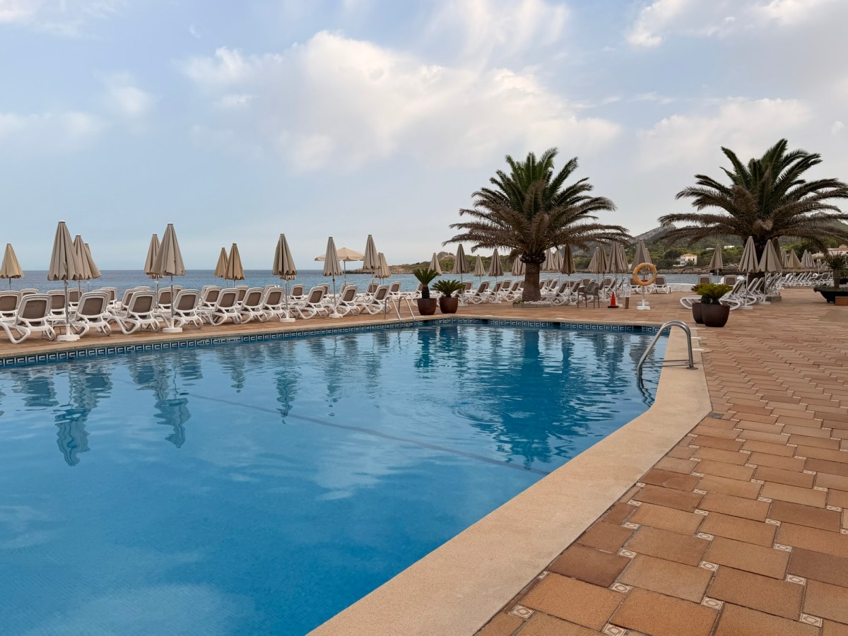 Scenic view of a swimming pool with palm trees and beach umbrellas.