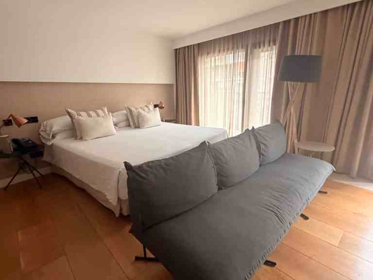 Elegant hotel room with large bed, sofa, and floor-to-ceiling windows.
