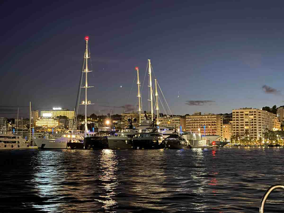 Marina at night with illuminated yachts and city skyline in the background.