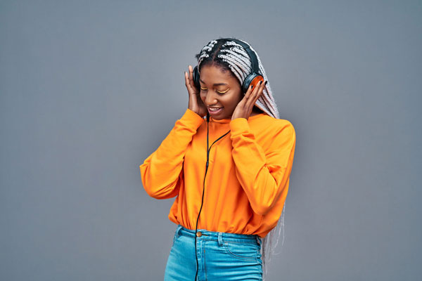 écouteurs sans fil portés par une femme souriante portant un sweat orange et un jeans, musique et mode, style décontracté, technologie haute qualité.