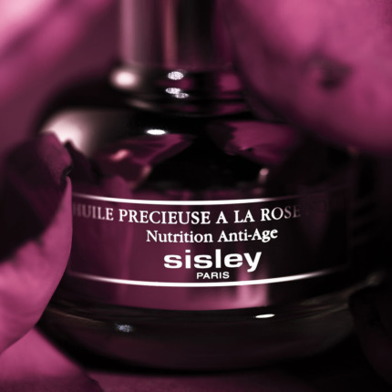 Lotion anti-âge Sisley Paris dans un flacon élégant, entouré de fleurs roses.
