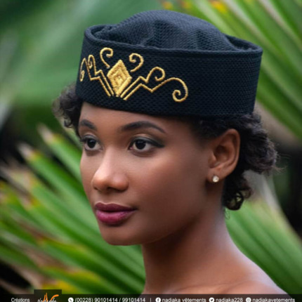 Chapeau traditionnel noir orné de broderies dorées porté par une femme avec fond végétal.