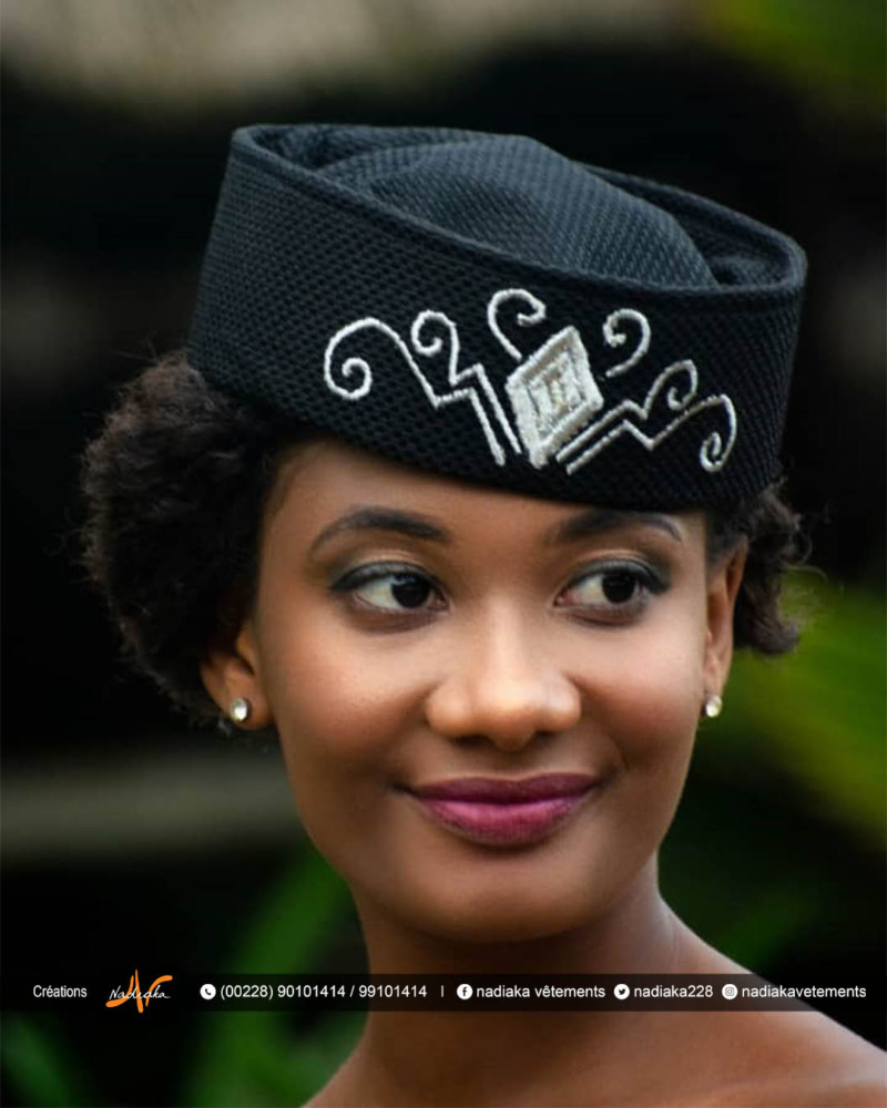 Élégante femme souriante portant un chapeau traditionnel noir avec broderie blanche.