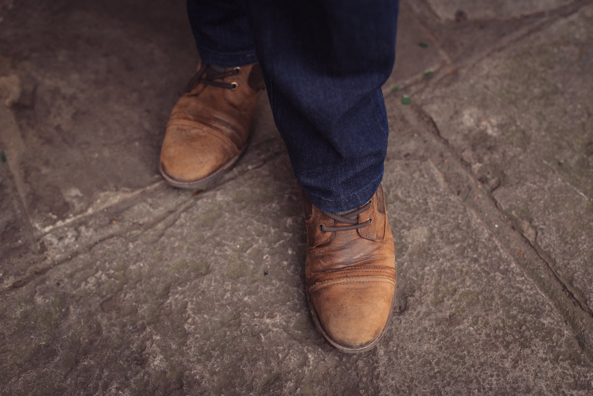 Clive Maxheath's smart brown leather brogues and dark denim trousers on a textured stone surface
