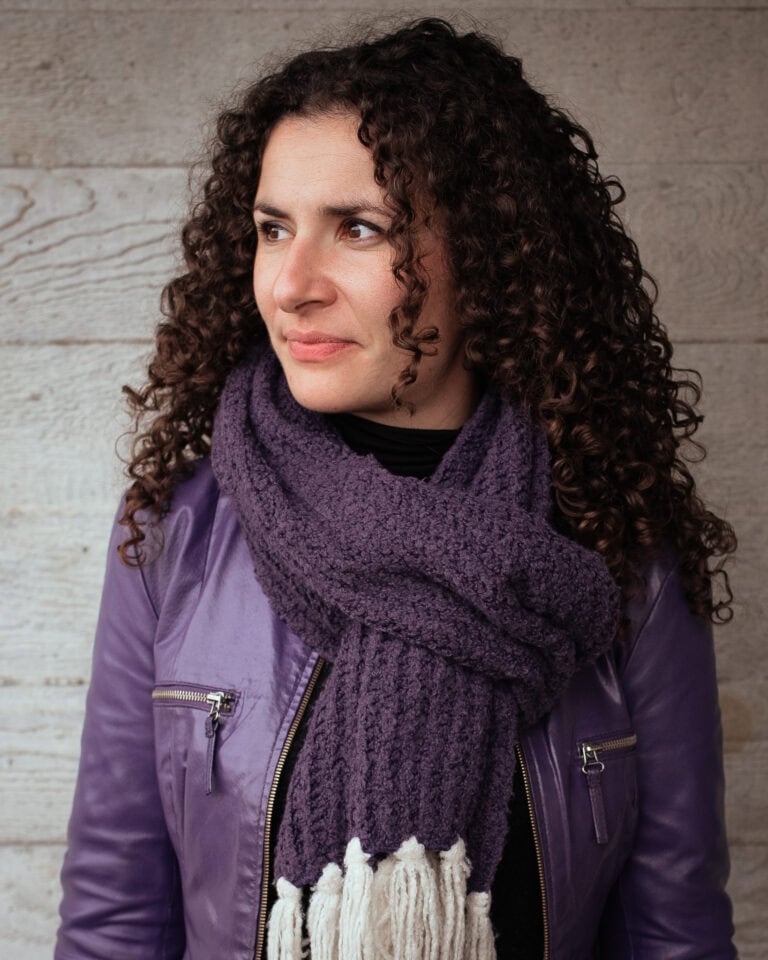 Valerie Teller, a confident woman with curly hair, wears a purple leather jacket and a textured scarf, photographed by a London brand photographer.