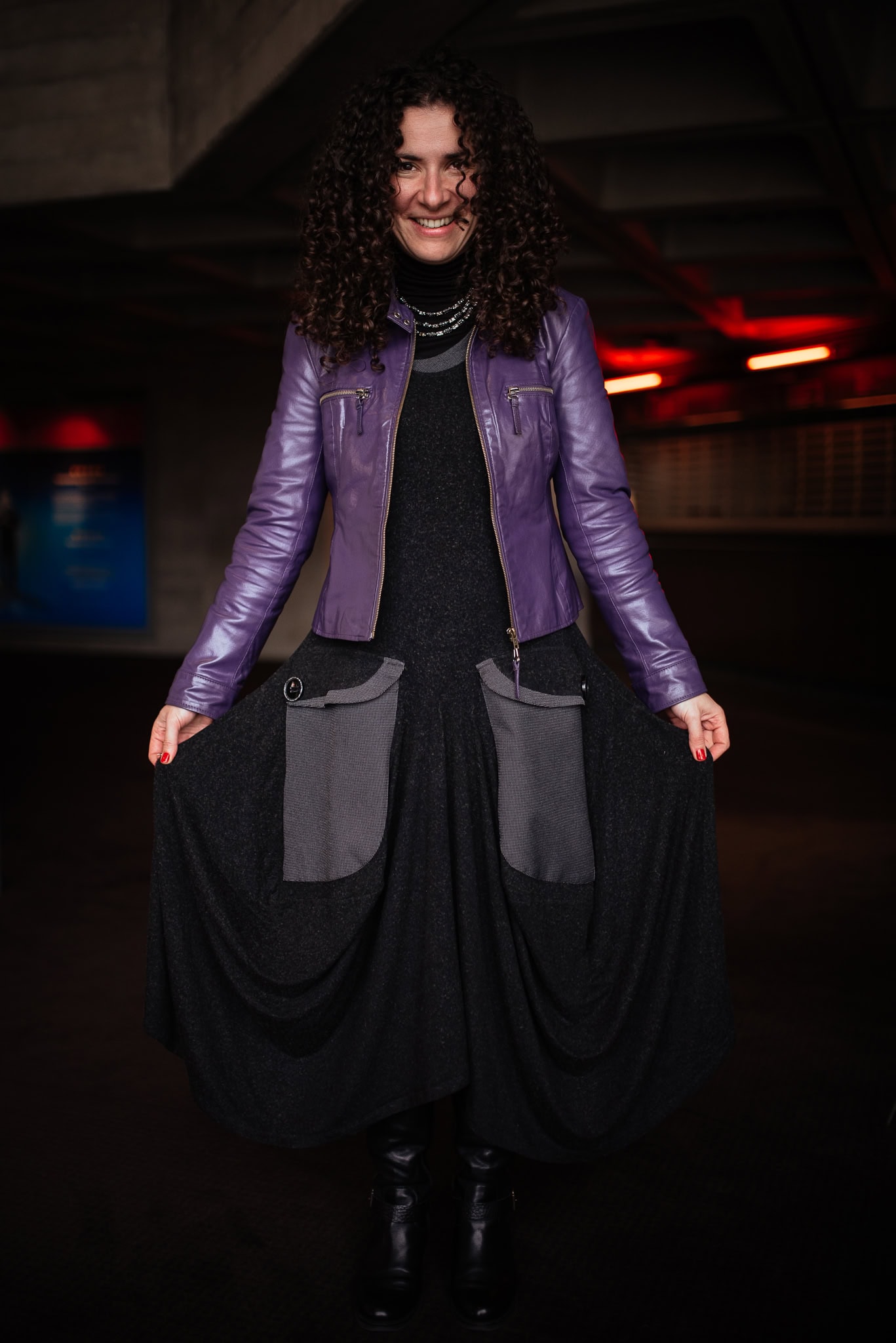 Valerie Teller, a stylish woman with curly hair, wears a purple leather jacket over a dark dress, showcasing her confident presence captured by a London brand photographer.