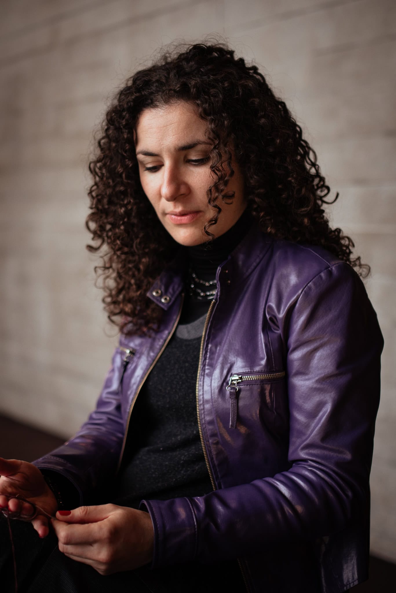 Valerie Teller, a woman with curly hair, wears a purple leather jacket and looks down thoughtfully.