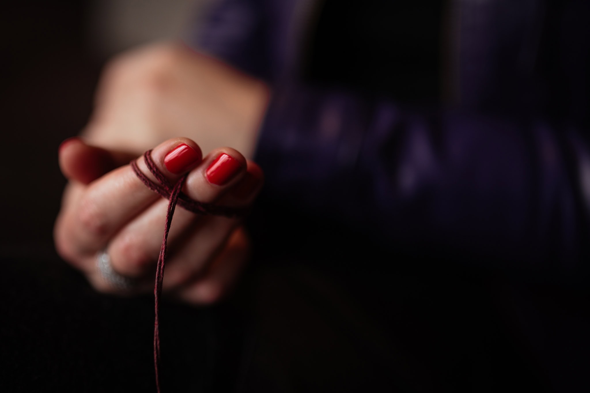 Valerie Teller's hands, adorned with red nail polish, delicately hold dark red yarn, hinting at creative craftsmanship.