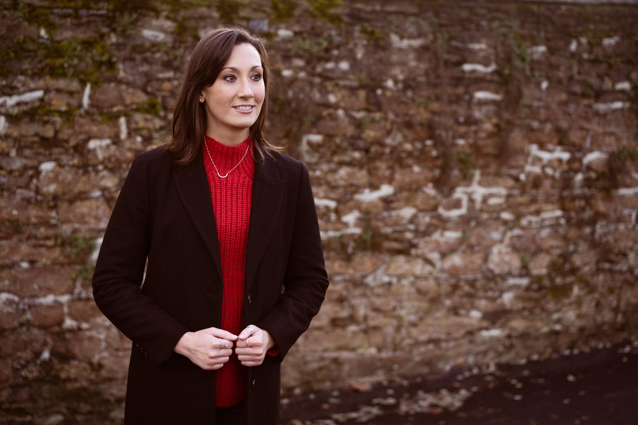 Jess Ratcliffe, a coach, in a thoughtful pose against a textured stone wall, captured by a London brand photographer.