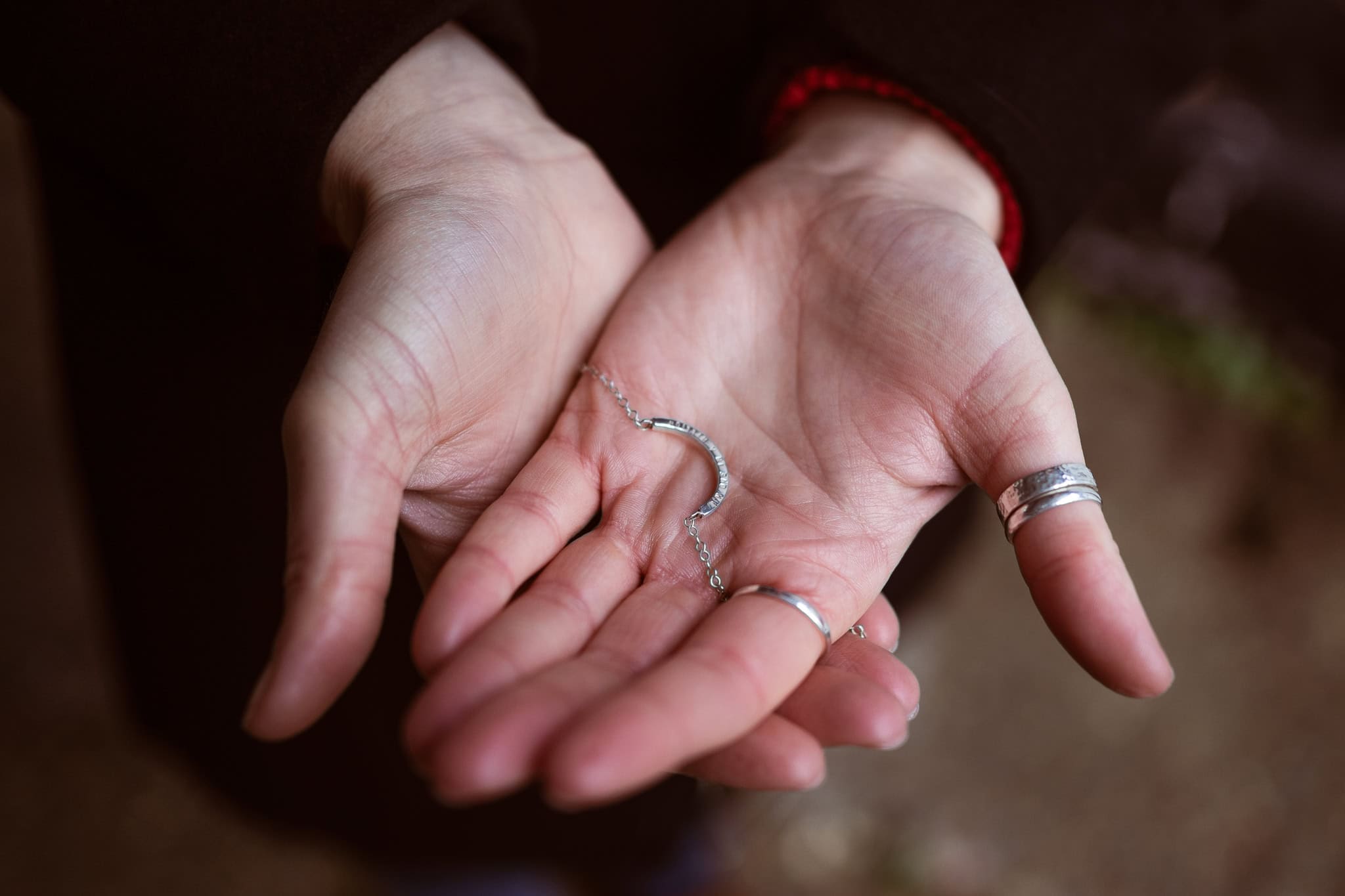 Jess Ratcliffe's hands gently hold a delicate silver necklace, adorned with rings.
