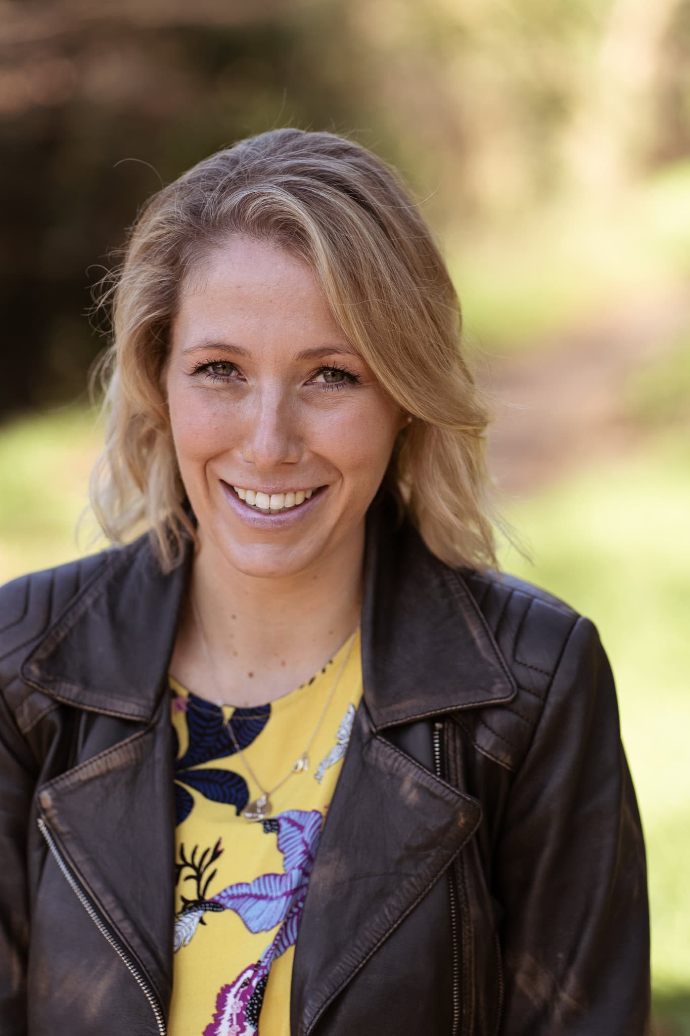 Jo Garside, coach, smiles warmly in natural light, wearing a leather jacket and floral dress.