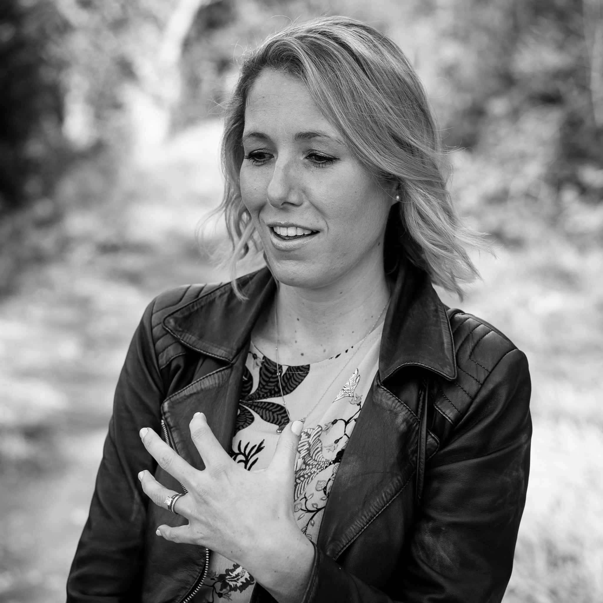 Jo Garside, a confident woman in a leather jacket, with her hand on her chest, captured in soft natural light.