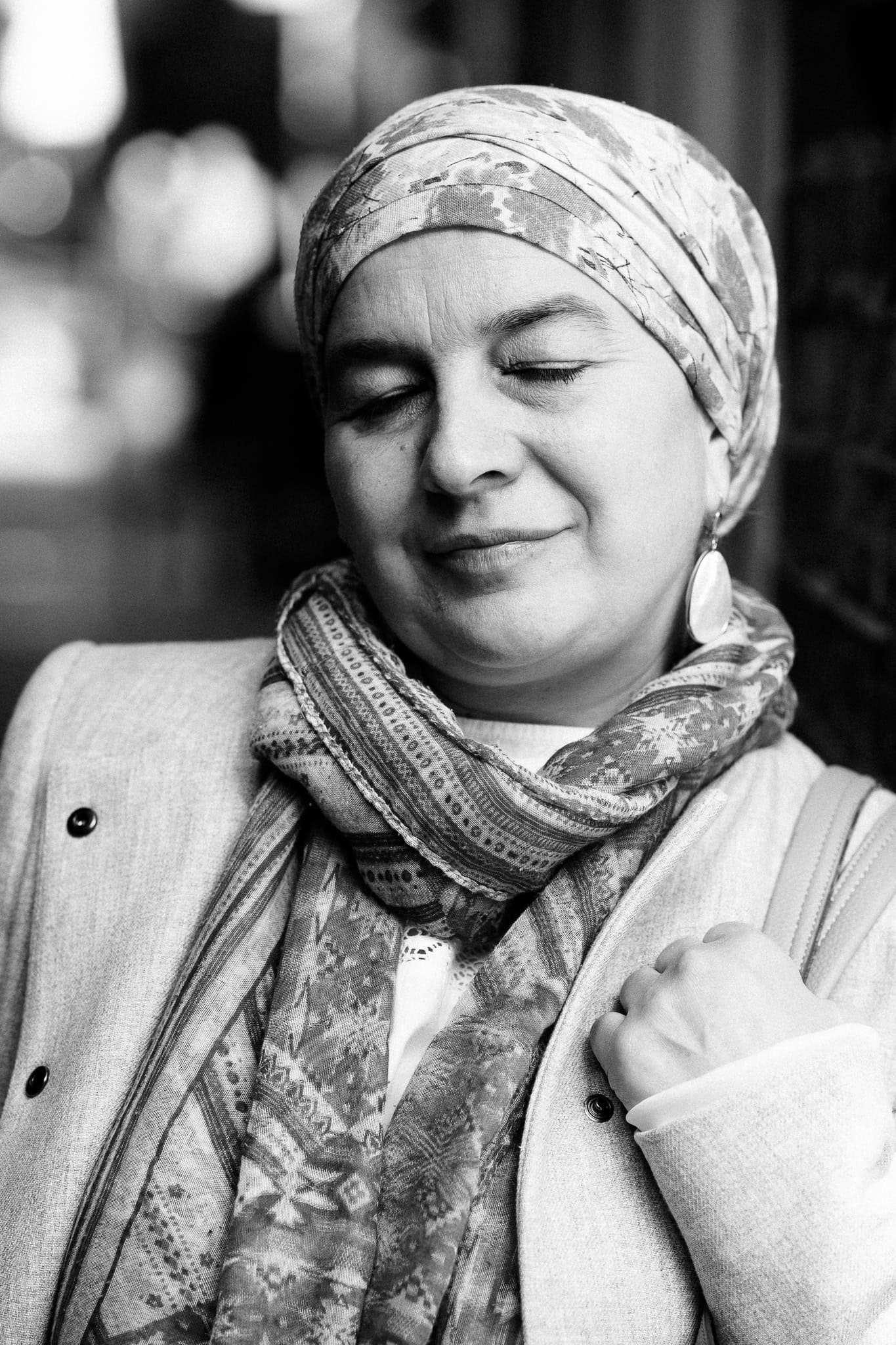 A warm, authentic portrait of a woman in a headscarf and scarf, eyes closed, in London. Shot by a London brand photographer.