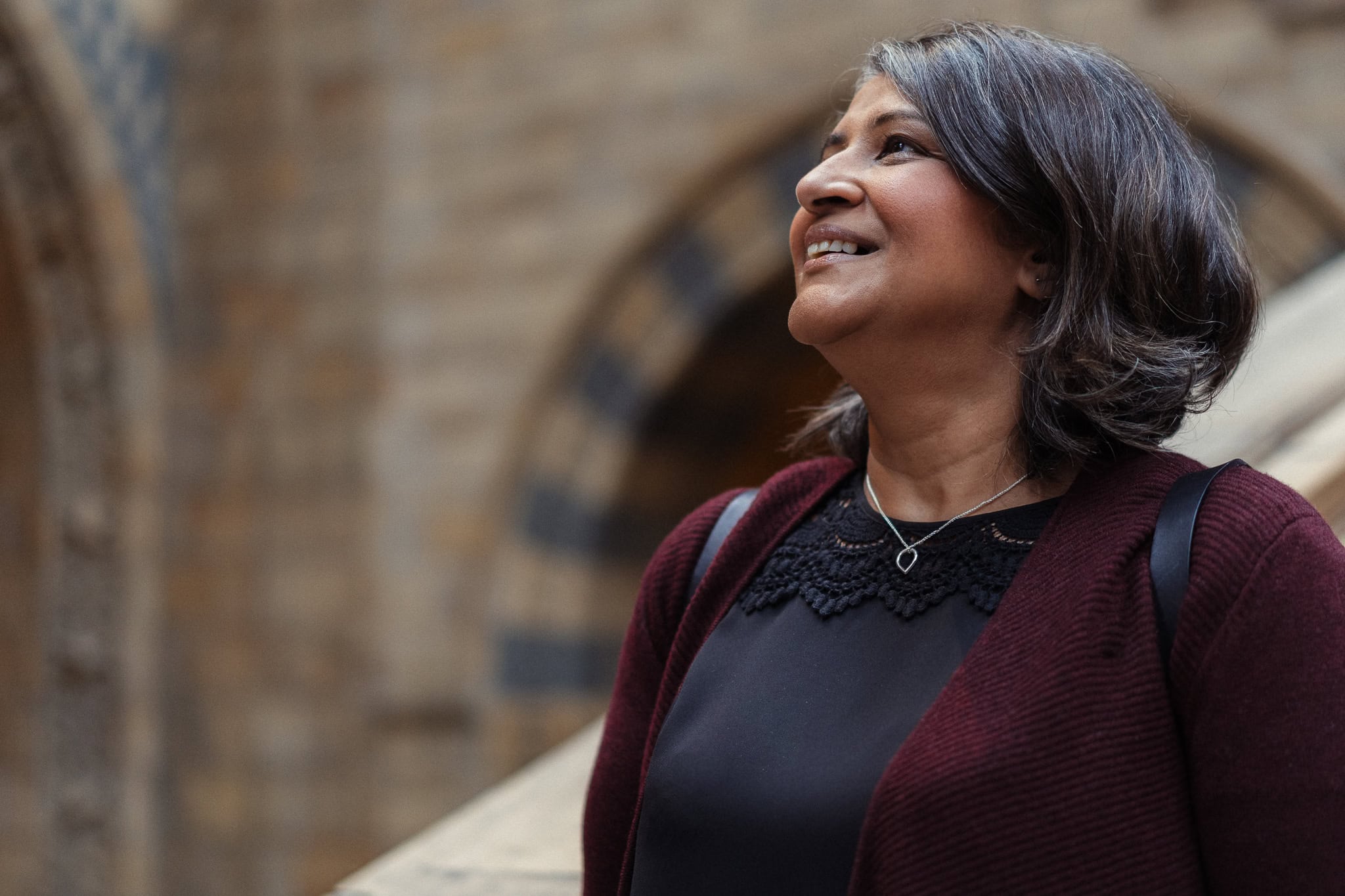 Anita Patel, a confident woman, smiles warmly in soft light, captured by a London brand photographer.