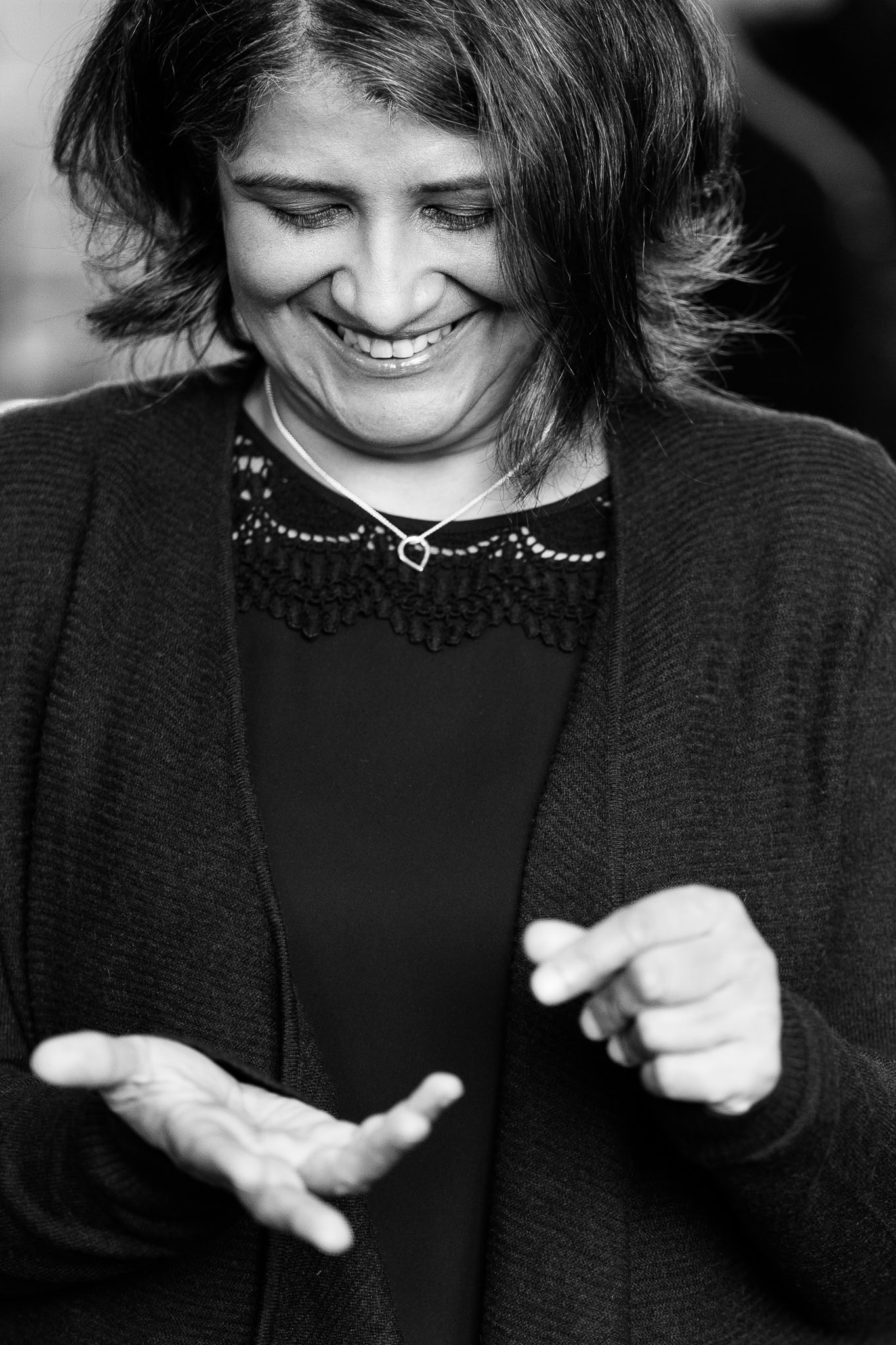 Anita Patel, a coach, smiles warmly while gesturing with her hands, captured in soft light by a London brand photographer.