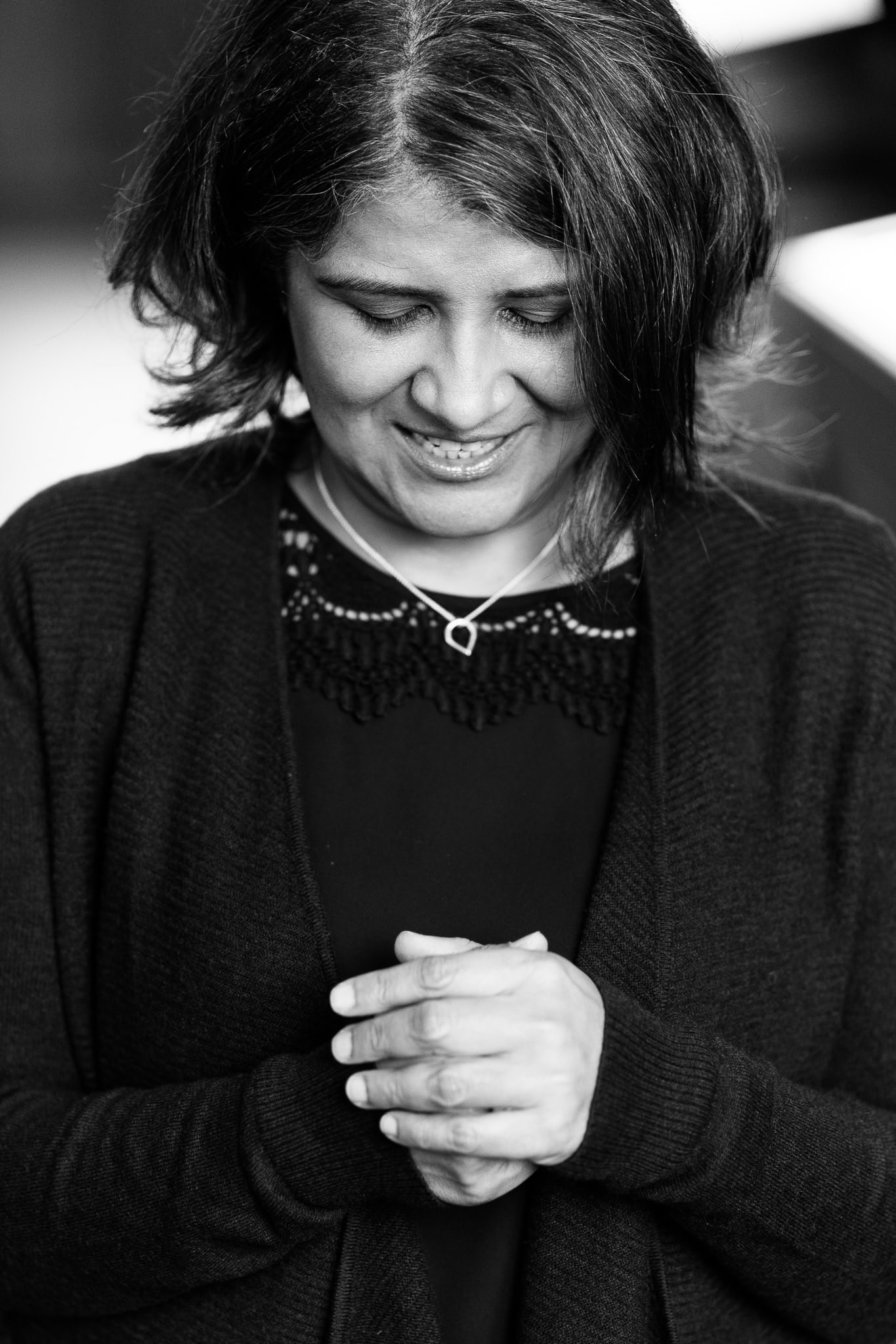 Anita Patel, a coach, looking down with hands clasped, captured by a London brand photographer.