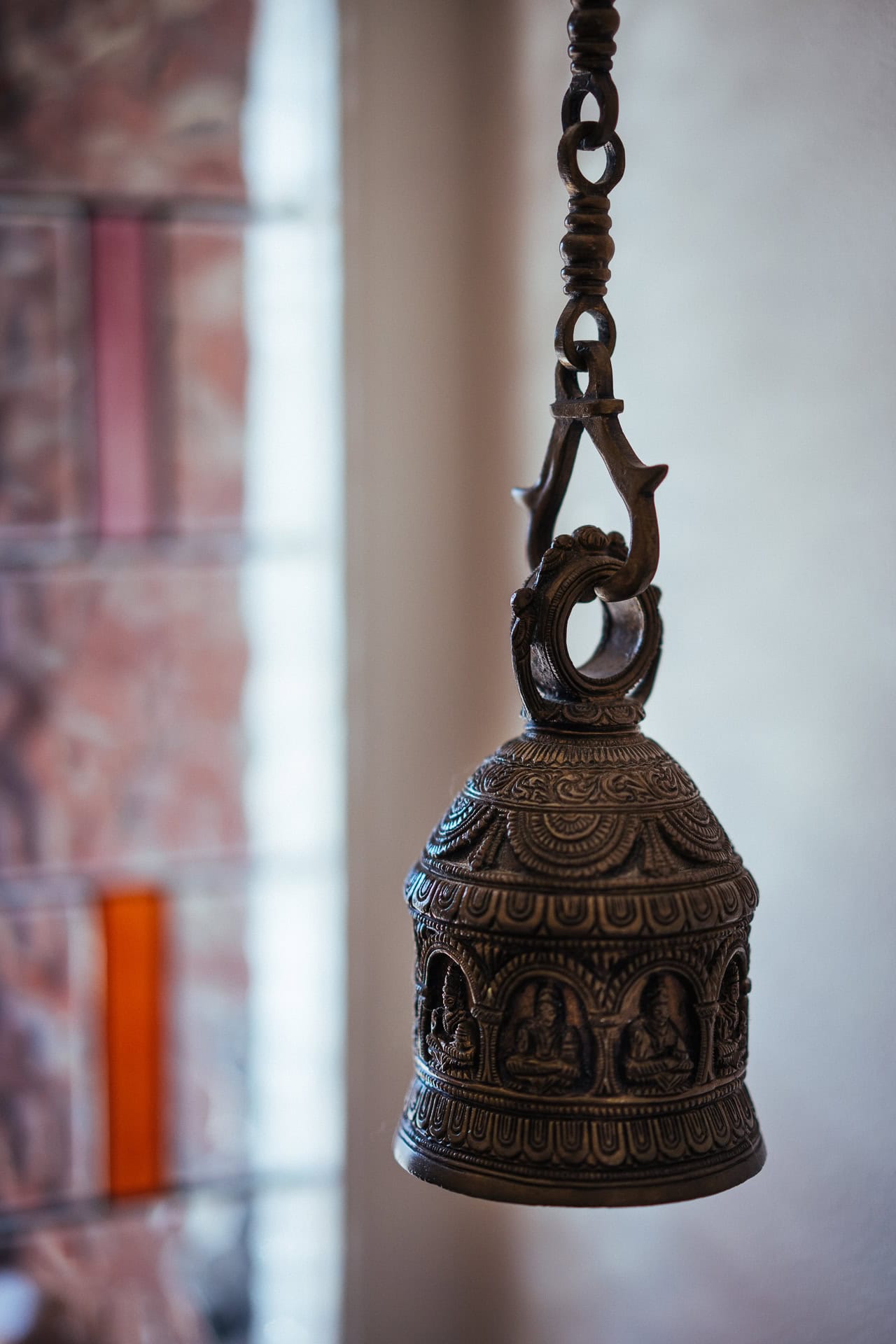 Ornate bronze bell with intricate carvings, possibly a temple bell, hanging from a decorative chain.