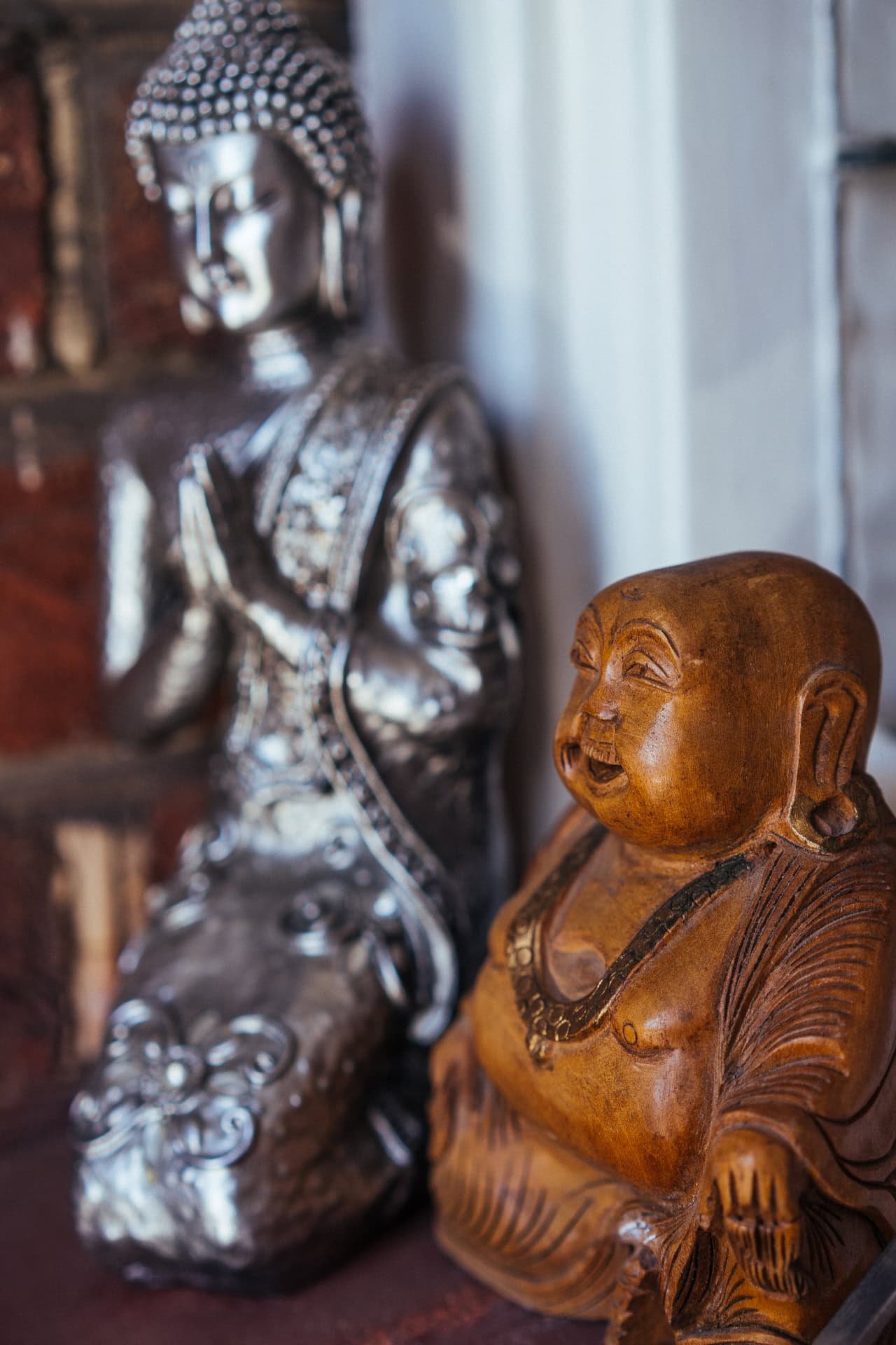 Wooden Buddha figurine in foreground, silver Buddha statue in background, London brand photography