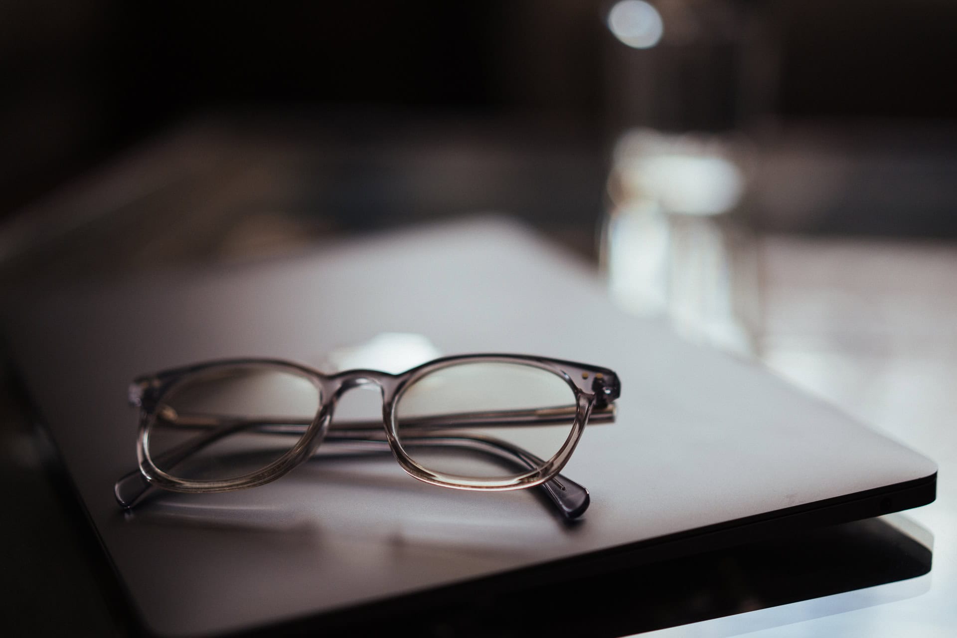 Dipak Dave's clear-framed glasses resting on a laptop, with soft lighting.
