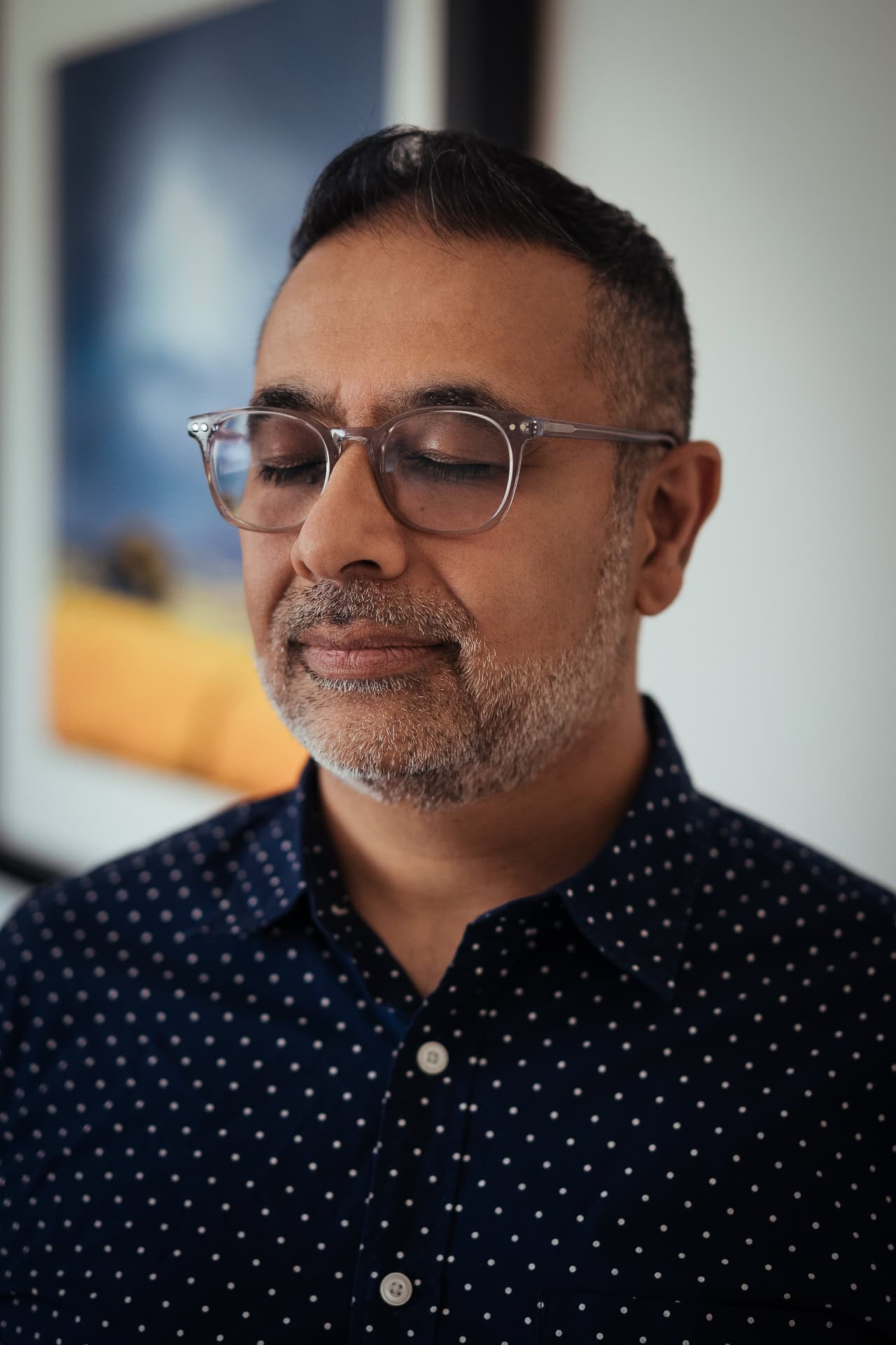 Dipak Dave, a man with a beard and glasses, with eyes closed, in a dark blue polka dot shirt.