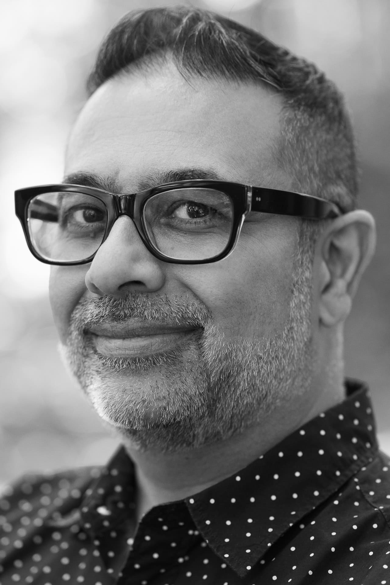 Dipak Dave, a London brand photographer, captured in a black and white headshot with glasses.