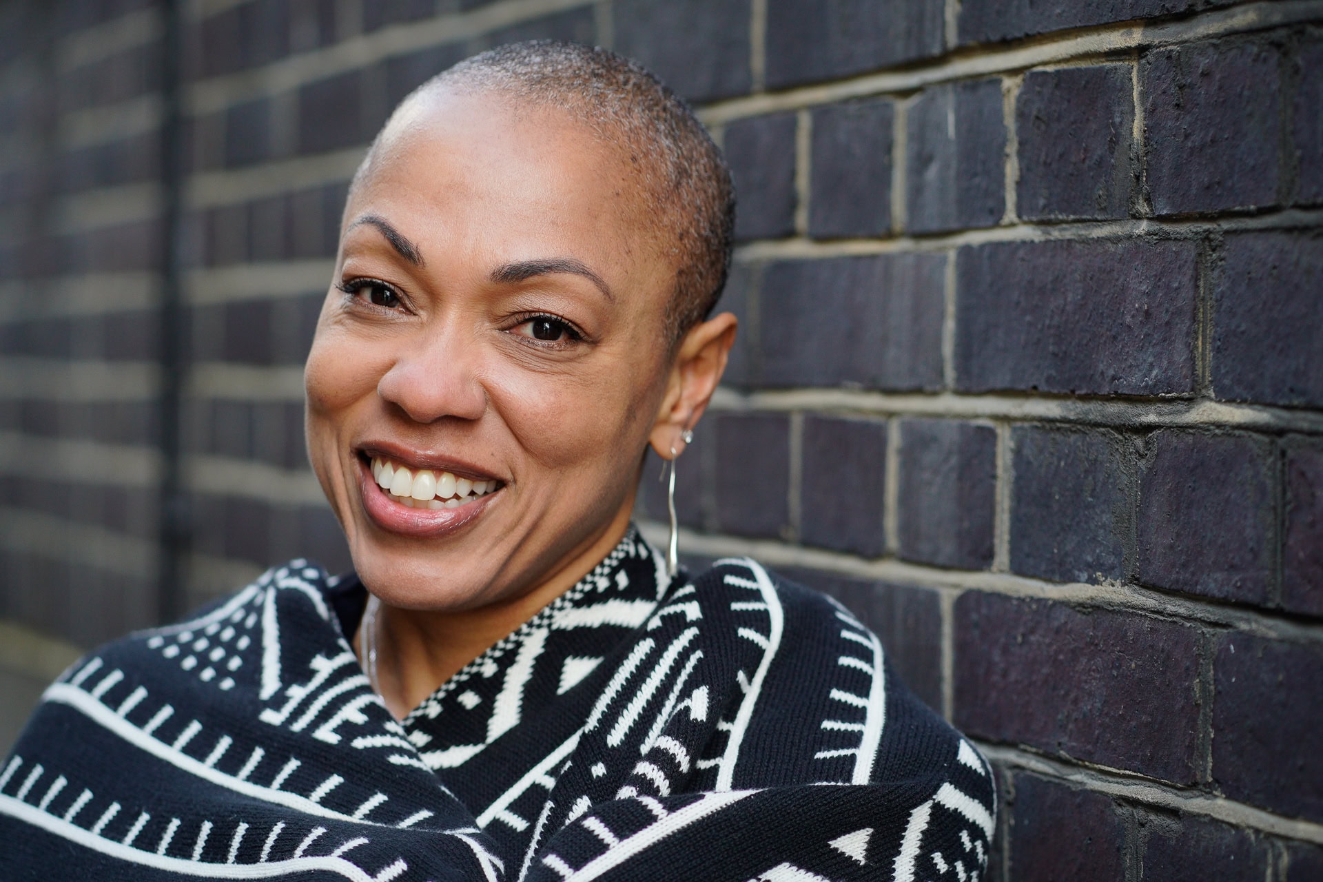 Sharlene Jones, a confident woman, smiles warmly against a London brick wall, captured by a London brand photographer.
