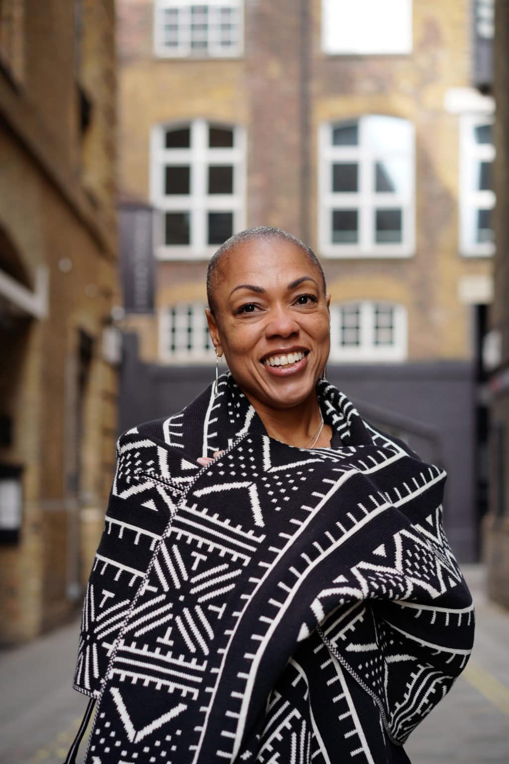 Sharlene Jones, a confident woman, smiles warmly in a London street, captured by a London brand photographer.