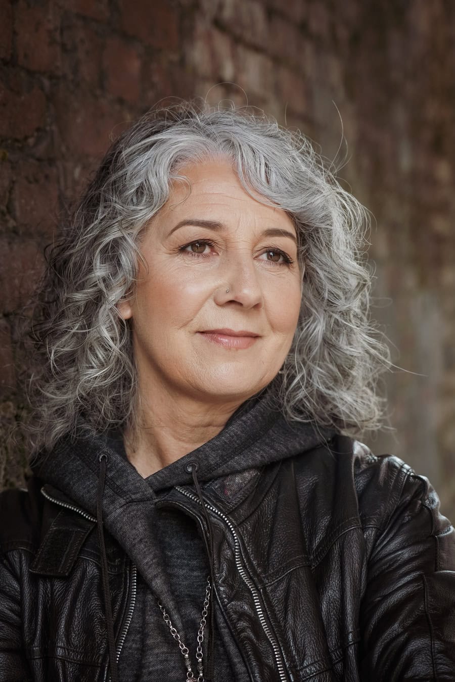 Zena Me, a confident woman with grey curly hair, in a leather jacket, captured by a London brand photographer.