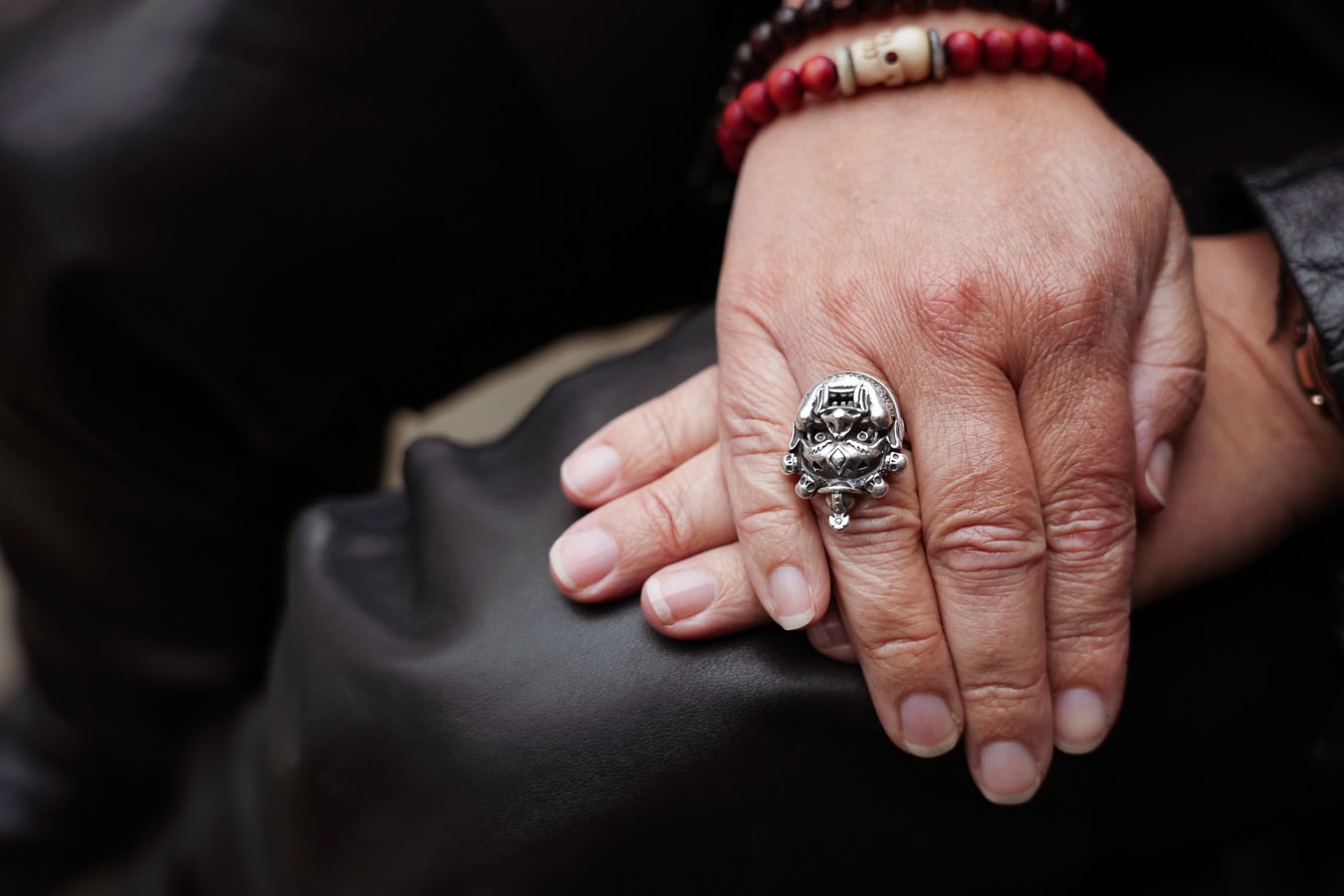 Close-up of a person's hand wearing a detailed silver skull ring and red beaded bracelets, captured by a London brand photographer.