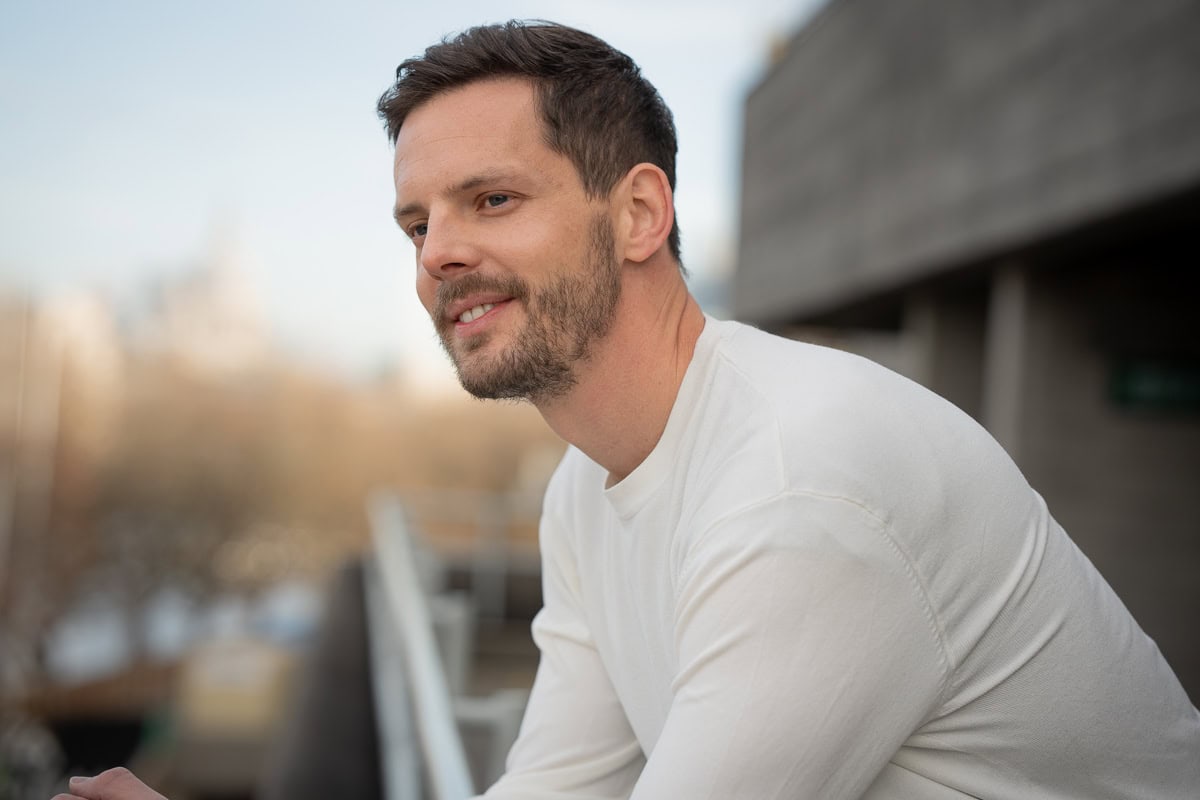 Cedric Boue, a man with a beard, smiles warmly in soft natural light with a blurred London backdrop.