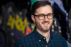Mark Leruste, a confident coach, smiles warmly in a London brand photography portrait with vibrant graffiti.