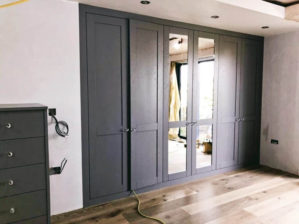 Custom grey fitted wardrobe with mirror doors for bespoke bedroom storage solutions.